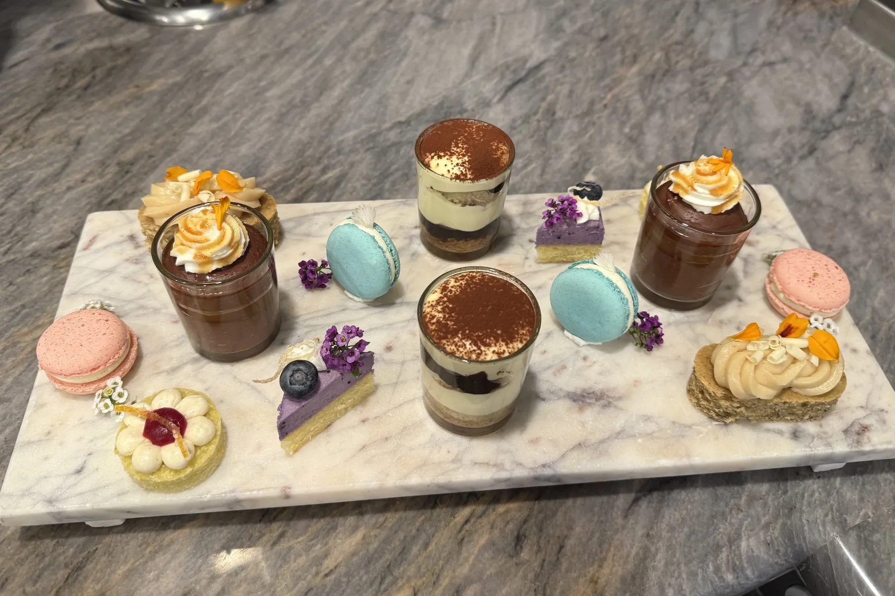 Marble tray of small desserts: tiramisu cups, chocolate pots with orange cream, macarons, and mini tarts