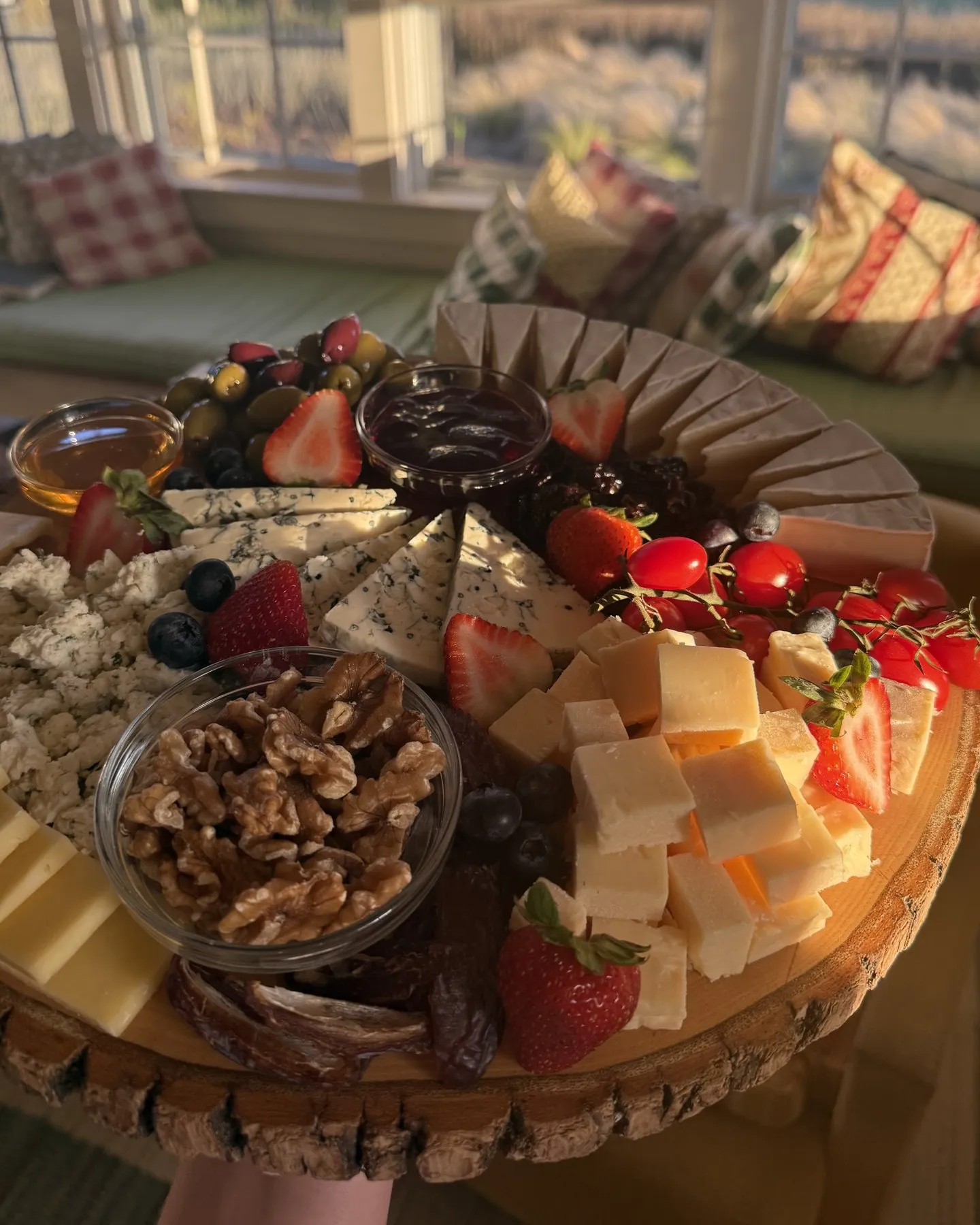 Round wooden board of cheeses, walnuts, strawberries, and cherry tomatoes in late afternoon window light